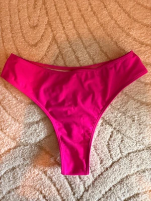 Rosa bikiniunderdel med hög midja - Säljer en snygg bikiniunderdel i stark rosa färg. Modellen har hög midja och en klassisk, enkel design utan mönster eller extra detaljer. Perfekt för strandhäng eller pooldagar i sommar. Helt oanvänd.
