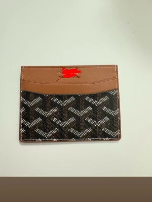 Brun och svart kortfodral i läder - Snyggt kortfodral i brunt och svart med grafiskt mönster. Fodralet har flera kortfack och är gjort i en kombination av slätt läder och canvas med vit kontrastsöm. Perfekt för dig som vill ha ett stilrent och praktiskt accessoar. Inte äkta och helt ny 