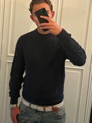 Kabelstickad tröja Selected - Snygg mörkblå kabelstickad tröja från Selected med tjock rund halsringning och ribbade muddar. Perfekt till jeans eller chinos för en clean och stilren look. Tröjan har ett klassiskt mönster och är tillverkad i mjukt material som känns skönt mot huden.
