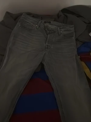 Jack & Jones  - Snygga gråa slim fit jeans med klassisk femficksdesign och dragkedjegylf. Jeansen har en tvättad look och raka ben, perfekta för en avslappnad stil. Passar till det mesta och är ett måste i garderoben.