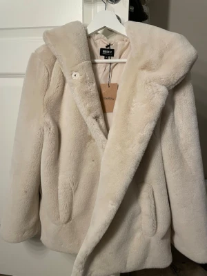 Beige jacka  - Mysig beige jacka från Bubbleroom med stor huva och dolda knappar framtill. Några defekter från tidig ägare men säkert går att få bort. Knappen längst ner är svår att knäppa