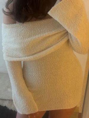 Krämvit offshoulder kortklänning - Säljer en krämvit, mjuk och fluffig kortklänning med offshoulder-design och långa ärmar. Klänningen har en avslappnad passform och är tillverkad i ett stickat material som känns riktigt mysigt. Perfekt för dig som gillar en enkel men ändå trendig look.storlek S-M