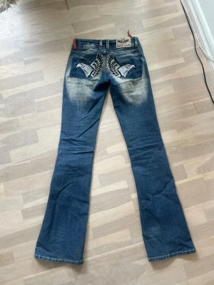 Blå bootcut jeans Crazy Age - Säljer ett par blå bootcut jeans från Crazy Age med vingar på bakfickorna. Jeansen har midje mått 35 och inerbens längd 83, säljer jeansen då dom blivit försmå för mig