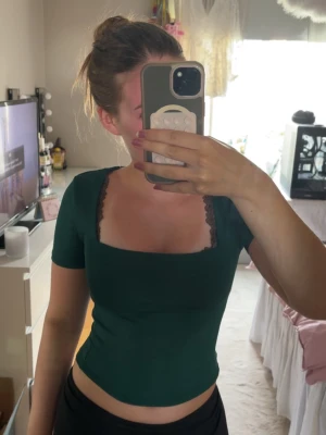 Grön topp/T-shirt från Amisu (New Yorker) - Mörkgrön croppad topp från Amisu med fyrkantig urringning. Kortärmad och figurnära passform, perfekt för dig som gillar en enkel men ändå snygg stil.