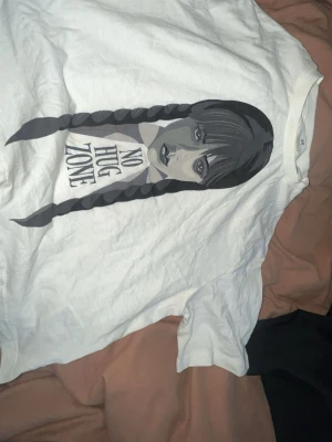 Vit t-shirt med tryck från H&M - Vit t-shirt från H&M med ett stort tryck av en tjej med flätor och texten 'NO HUG ZONE' på framsidan. Klassisk rund hals och korta ärmar. Perfekt för dig som gillar statement-plagg och grafiska motiv.