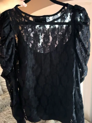 Svart spetsblus  - Säljer en svart blus i spets med puffiga långärmar och rund halsringning. Blusen har ett elegant blommigt mönster i spetsen med ett avtagbart linne. Aldrig använd 