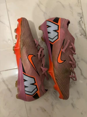  Nike Mercurial Vapor 16 Elit - Säljer ett par Nike Mercurial fotbollsskor i rosa med orange och svart detalj. Har använt dessa skor i Ca 4-5 Månader. Lite slitna som ni kan se på vissa bilder men annars funkar de perfekt. Snöret på höger skon har hoppat av men går nog att fixa annars brukar jag lägga snöret inne i skon. Om ni vill ha en Nyare/Fräschare look så kan ni gärna tvätta de. Köpt från Unisport för 2879kr. Original påse medföljs! Hör av er gärna vid intresse. Fraktar samma dag eller dagen efter😀