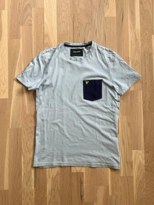 Lyle & Scott T-shirt – Storlek S – Nyskick - Säljer en stilren Lyle & Scott T-shirt i storlek S. Ljusblå med mörkblå bröstficka och broderad Lyle & Scott-logga.  * Storlek: S * Skick: Nyskick * Färg: Ljusblå/mörkblå * 100 % bomull * Mycket bekväm och passar både till vardag och finare tillfällen.  Pris: 249 kr.