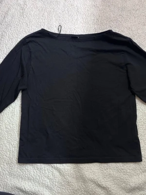 Svart långärmad topp i bomull - En enkel svart långärmad topp med rak passform och rund halsringning. Tillverkad i mjuk bomull, perfekt att styla med jeans eller kjol. Klassisk och tidlös design som funkar till många olika looks.