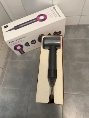 Dyson Supersonic hårfön lila/vit - Säljer en Dyson Supersonic hårfön i lila och vitt. Kommer i originalförpackning med flera magnetiska stylingmunstycken för olika hårtyper. Designad för snabb torkning utan extrem värme och ger ett slätt resultat. Perfekt för dig som vill ha salongskänsla hemma.