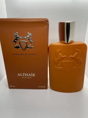 Parfums de Marly Althaïr EdP 125ml - Exklusiv parfym från Parfums de Marly, Althaïr Eau de Parfum. Flaskan är matt orange med silverfärgat lock och har ett elegant reliefmönster med två hästar och sköld. Förpackningen matchar flaskans färg och design. Innehåller 125 ml, nypris 3499kr