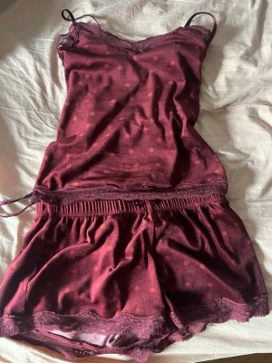 Vinrött spetskantat underklädesset - Sött vinrött underklädesset med linne och shorts. Setet har tunna axelband, spetsdetaljer vid urringning och benslut samt diskret prickmönster över hela tyget. Från hunkemöller, toppen är storlek xs och shortsen storlek M!