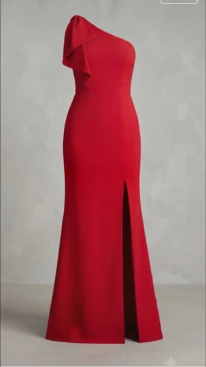 Röd långklänning med slits - Elegant röd långklänning med oneshoulder och slits framtill. Klänningen har en figurnära passform och ett stilrent, minimalistiskt uttryck. Perfekt för dig som vill sticka ut med en klassisk och sofistikerad look.