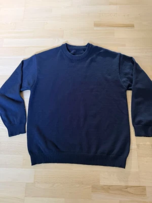 Mörkblå stickad tröja  - En enkel och stilren mörkblå stickad tröja med rund halsringning och ribbade muddar vid ärmslut och nederkant. Perfekt basplagg för lager på lager och passar till det mesta. Materialet känns mjukt och bekvämt.