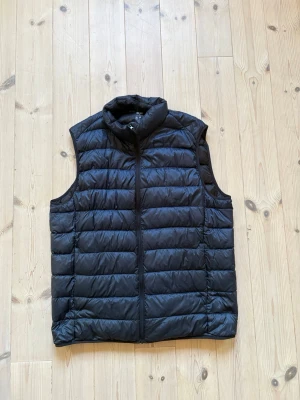 Marinblå dunväst från Uniqlo - Säljer en marinblå, lätt och smidig dunväst från Uniqlo. Västen har quiltad design, hög krage och dragkedja framtill. 