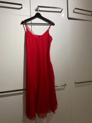 Röd långklänning med tunna axelband - Säljer en röd långklänning med tunna axelband och lätt vågig nederkant. Klänningen har en enkel, elegant siluett och är tillverkad i ett tunt, flytande material som ger ett mjukt fall. Från HM