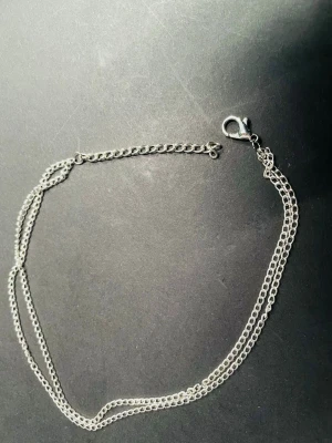 By prisförslag- dubbel silverfärgad fotlänk  - En enkel och stilren tunn fotlänk i silverfärg med dubbla länkar. Kedjan har ett klassiskt karbinlås och justerbar längd. Passar perfekt som diskret accessoar eller för lager-på-lager-stil. Finns också i guld.