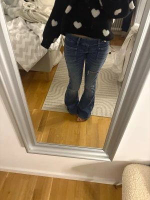 Blå bootcut jeans med slitningar - Snygga blå bootcut jeans med slitningar på knäna och låren. Jeansen har klassisk femficksmodell och låg midja. Perfekta för en avslappnad och trendig look. Materialet är denim i bomull.