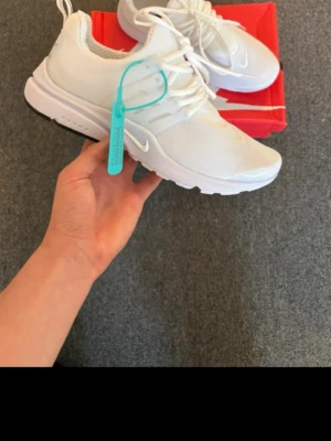 Nikw prestos  - Säljer ett par fräscha vita Nike Air prestos med mesh-överdel och vita snören. Skorna har en clean look med diskret Nike-logga på sidan och en blågrön tag på ena skon. Perfekta för dig som gillar stilrena och sportiga sneakers.
