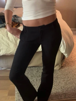 Svarta kostymbyxor med rak passform - Snygga svarta kostymbyxor med rak passform och normal midja. Byxorna har diskreta fickor fram och stängs med knapp och dragkedja. Perfekta för en clean och stilren look. Materialet ser ut att vara en mjuk och lätt vävd kvalitet.