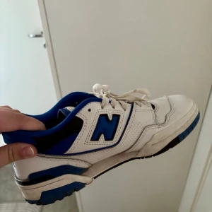 New Balance 550 skor  - New balance 550 sneakers i vitt och blått storlek 38,5. Skorna har vita snören, blå detaljer och svart sula med blå inslag. Ovandelen är i läder och designen är sportig med lågt skaft. Perfekta för dig som gillar retrostil och streetwear. Köpta från Vallgatan 12 i Göteborg 💙