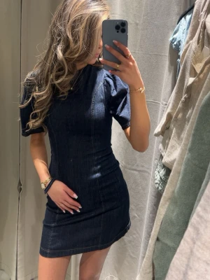 Mörkblå jeansklänning med puffärm - Snygg och jättesöt mörkblå kort jeansklänning med puffärmar och figurnära passform. Klänningen har markerade sömmar och rund halsringning, vilket ger en trendig och stilren look. Helt nytt, aldrig använd med prislapp på