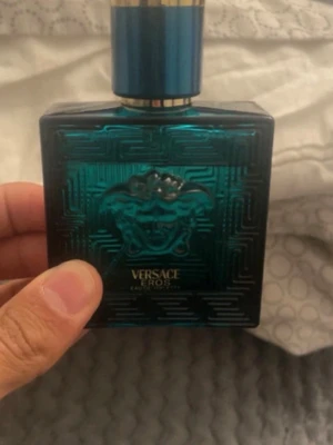 Versace Eros Eau de Toilette - Versace Eros Eau de Toilette i en snygg turkosblå glasflaska med Medusa-huvudet i relief på framsidan. Flaskan har en fyrkantig form och ett blått lock med gulddetaljer. En ikonisk doft som sticker ut både i design och känsla.