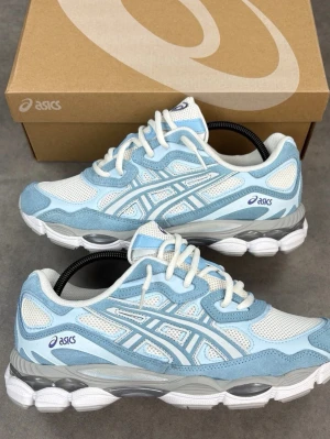  Nya Asics sneakers i blått och vitt - Snygga Asics sneakers i ljusblått och vitt med mesh- och mockadetaljer. Skorna har en chunky vit och grå sula, klassiska Asics-loggor på sidan och vita skosnören. Perfekta för dig som gillar sportig och trendig stil.