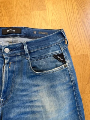 Blå Replay Anbass jeans herr - Säljer ett par blå Replay Anbass jeans i klassisk slim fit-modell. Jeansen har snygga slitningar och tvättade detaljer framtill, fem fickor och silverfärgad knapp. Perfekta för dig som gillar en avslappnad men trendig look.