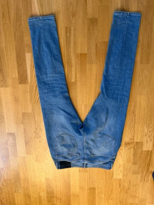 Blå raka jeans med hög midja - Säljer ett par klassiska blå jeans med raka ben och hög midja. Jeansen har två bakfickor och bälteshällor. Materialet är denim i 100% bomull och färgen är ljusblå med lätt tvättad look. Perfekta till en avslappnad stil. 