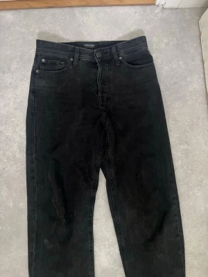 Svarta raka jeans från JACK&JONES - Säljer ett par svarta jeans från JACK&JONES med rak passform och klassisk femficksdesign. Jeansen har knappgylf och är tillverkade i ett mjukt denimtyg som ger en avslappnad look. Perfekta till en streetwear-outfit.