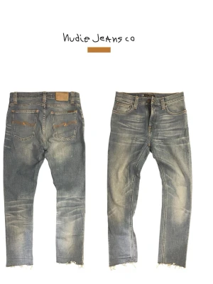 Blå slitna jeans från Nudie Jeans - Ett par blå jeans från Nudie Jeans med slitna detaljer och råa kanter vid bensluten. Jeansen har klassisk femficksdesign, kontrastsömmar och en tvättad look med ljusa partier. Tillverkade i denim, perfekt för en avslappnad stil.