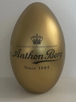 Guldägg från Anthon Berg - Snyggt guldägg från Anthon Berg, perfekt som present eller dekoration. Ägget är gyllene och har elegant svart text med logga och krona. Tillverkad i metall och har en lyxig känsla. Passar bra till påsk eller som samlarobjekt.