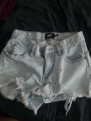 Ljusblå denimshorts med fransar - Säljer ett par ljusblå denimshorts från 157 med råa, fransiga kanter och klassisk femficksdesign. Shortsen har normal passform och midwaist. Perfekta för varma dagar och en avslappnad stil.