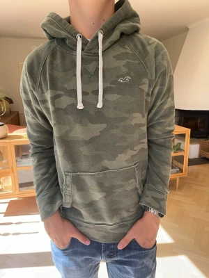 Hollister hoodie militär grön herr vintage - Hollister camo hoodie 🪖 Snygg camouflagefärgad hoodie från Hollister med diskret broderad Hollister-logga på bröstet. Mjuk och bekväm modell med huva, vita snören och magficka. Perfekt till en casual/streetwear-look. Fint skick!  #Hollister #HCO #HollisterHoodie #Camo #Camouflage #Hoodie #Streetwear #Y2K #Menswear #Preppy #Vintage #Casual