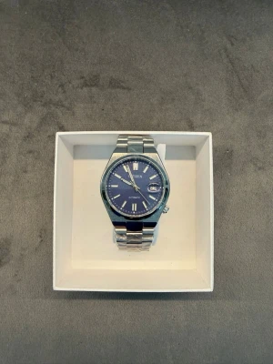 Citizen klocka med blå urtavla - Snygg Citizen klocka med blå urtavla och silverfärgad länk i metall. Klassisk design med datumvisning och tydliga indexmarkeringar. Perfekt accessoar för dig som gillar stilrena detaljer och tidlös look.