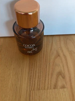 Cocoa Sunset parfym från Zara - Cocoa Sunset parfym från Zara i en rund, brun glasflaska med elegant roséguldfärgat lock. Flaskan har en modern och stilren design som känns lyxig och trendig. Perfekt för dig som gillar varma och söta dofter.