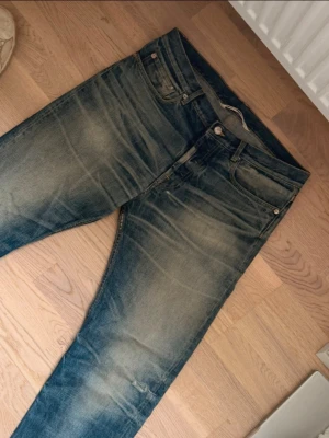 Blå slitna jeans med raka ben - Säljer ett par blå jeans med snyggt sliten tvätt och raka ben. Jeansen har klassisk femficksdesign, normal midja och detaljerade slitningar på bakfickorna. Perfekta för en avslappnad och trendig look. Storlek: W31 