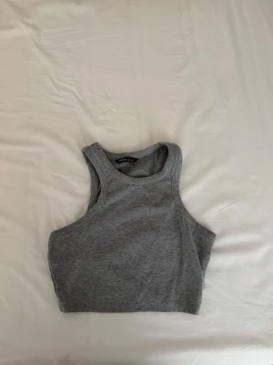 Grå ribbad linnetopp från SHEIN - Säljer en grå ribbad linnetopp från SHEIN i storlek S. Toppen är ärmlös och croppad med rund halsringning och stretchigt material som sitter snyggt på kroppen. Perfekt att matcha med jeans eller kjol för en trendig look.