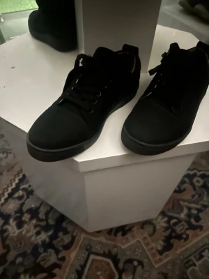 Svarta höga sneakers med snörning - Säljer ett par svarta christian louboutin utan nitar mocka  endas använd en gång  med högt skaft och klassisk snörning. Skorna har en stilren design och är tillverkade i ett matt material som ger en clean look. Perfekta för dig som gillar enkel och tidlös stil.