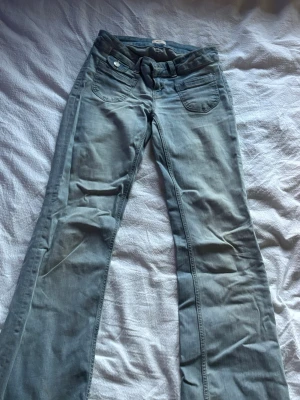 Ljusblå bootcut jeans med broderad ficka - Säljer ett par ljusblå bootcut jeans med snygga detaljer och broderad bakficka. Jeansen har klassisk femficksmodell och är tillverkade i mjukt denimtyg. Perfekta för dig som gillar en avslappnad men trendig stil. De har en liten fläck på knät (inget man tänker på särskilt mycket) men därav priset.