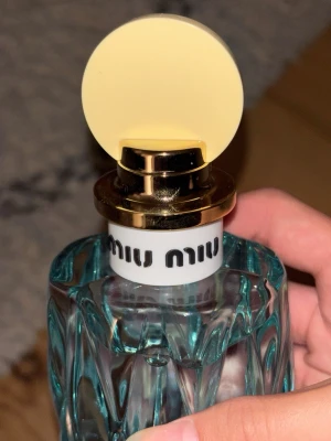 Miu Miu Eau de Parfum 50ml - Snygg parfymflaska från Miu Miu med en unik, blågrön glasdesign och rund, gul kork i plast och metall. Flaskan har en modern och lekfull look med Miu Miu-loggan tryckt på halsen. Perfekt för dig som gillar trendiga och exklusiva dofter.               somrig och tropisk doft, kommer med förpackningen ❤️. köpt för 1299kr