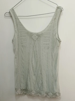 Ljus-mint topp med pärlbroderi - Supersöt linnetopp med pärlor och broderade mönster framtill i typ art nouveau stil. Toppen är ärmlös och har en feminin, med dekorativa kanter nertill. Perfekt att styla med jeans, kostymbyxor eller kjol för en trendig vibe. Se mått på bilder och se gärna mina andra annonser <3
