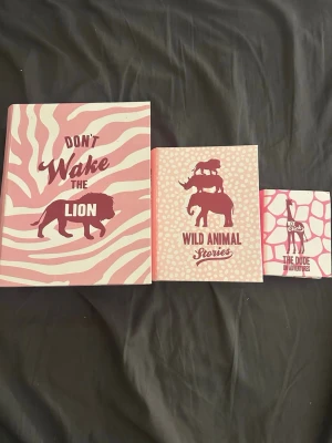 Set med tre rosa djurböcker - Tre böcker med djurtema och grafiska omslag i rosa och vitt. Titlarna är 'Don't Wake the Lion', 'Wild Animal Stories' och 'The Dude Adventures'. Omslagen har zebramönster, djursilhuetter och giraffmönster. Perfekt för dig som gillar djur och snygg design.