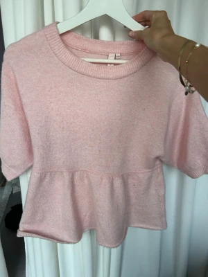 Ljusrosa stickad topp med volang - Superfin ljusrosa stickad topp med korta ärmar och volang nedtill. Mjuk och skön, perfekt till jeans eller kjol. Rund halsringning och avslappnad passform ger en söt och trendig look.