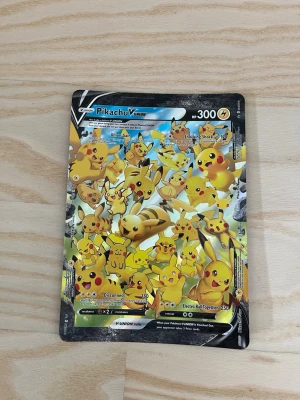 Pokémonkort Pikachu V-Union - Unikt Pokémonkort med Pikachu V-Union-motiv. Kortet har en färgstark design med flera Pikachu i olika poser och HP 300. Baksidan har klassiskt Pokémon-utseende med Pokéboll. Perfekt för samlare eller Pokémonfans.