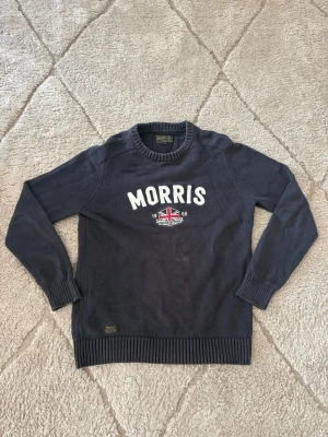 Mörkblå stickad Morris-tröja  - Säljer en riktigt snygg och skön stickad tröja från Morris Stockholm i mörkblått. Har ett snyggt tryck/broderi framtill med "MORRIS" och den klassiska Union Jack-loggan!  Märke: Morris Stockholm  Färg: Mörkblå (Navy) med vitt tryck och flaggdetalj  Modell: Stickad tröja / Crewneck  Storlek: M (syns på nacklappen)  Skick: Fint skick / sparsamt använd (justera om det finns något slitage) skriv om ni vill ha mått! 