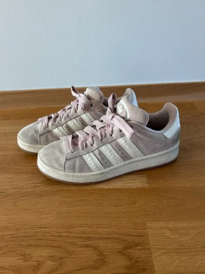 Adidas Originals Campus 00s - Snygga sneakers i ljusrosa mocka med ljusrosa skosnören och vita detaljer på sidorna. Klassisk låg modell med rund tå och vit sula. Perfekta för dig som gillar en stilren och trendig look. Passar till det mesta och är riktigt bekväma.