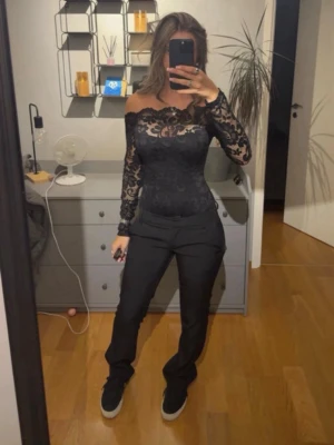 Svart spets offshoulder topp - Säljer en svart offshoulder topp i spets med lång ärm och transparenta detaljer. Toppen är tight och har ett elegant mönster över hela tyget, perfekt för dig som vill sticka ut lite extra.