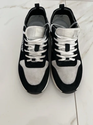 Svarta och vita sneakers - Snygga sneakers från adnes i svart och vitt med mesh- och mockadetaljer. Skorna har vita snören, logomönster på sidan och en chunky vit sula. Perfekta för dig som vill ha en exklusiv och trendig look.